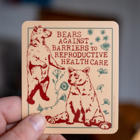a hand holding one sticker with the text Bears Against Barriers to Reproductive Healthcare